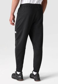 Czarne spodnie dresowe z elastycznym pasem, zwężanym krojem i zamykanymi na zamek kieszeniami. Wykonane z gładkiego materiału o subtelnym połysku.