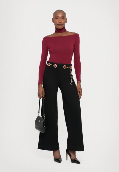 Bordeaux aansluitende coltrui, zwarte wijde broek met gouden ronde hardware en kettingdetail, gecombineerd met puntige zwarte hakken en een kleine tas.