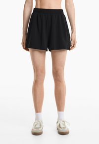 Zwarte sportieve shorts met een elastische tailleband, voorzien van zijzakken en knoopaccenten aan de zoom. De stof lijkt soepel en lichtgewicht.