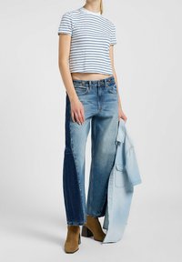 T-shirt blanc coupé avec des rayures marine, associé à un jean bicolore en denim clair et foncé. Bottes à talons brunes, veste légère.