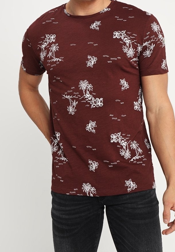 T-shirt en coton marron foncé avec un motif blanc de fleurs et de palmiers. Manches courtes et col rond renforcent son style décontracté.