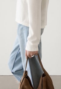 Maglietta bianca a maniche lunghe, jeans azzurri chiari, tiene una borsa in suede marrone. Dettagli notevoli: anello in argento e morbidezza del tessuto.