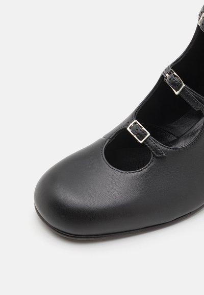 Černá kožená bota s kulatou špičkou, výřezovým designem a dvěma kovovými sponami na popruzích. Hladký povrch a nízký profil podešve.