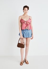 Camisola rosa a fantasia con strati a volant, abbinata a una gonna di denim e una borsa marrone. Sandali alti con cinturini marroni.