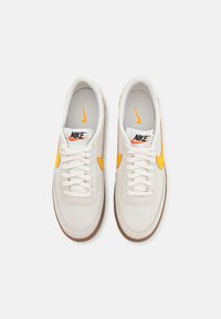 Bílé tenisky Nike s žlutými akcenty, hladký semišový povrch, klasický šněrovací design a texturovaná gumová podrážka.