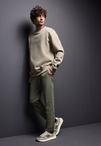 Beige mikina s žebrovanými manžetami, zdobená nenápadným textem. Olivově zelené kalhoty s volným střihem. Šedé a bílé tenisky s texturovanými detaily.