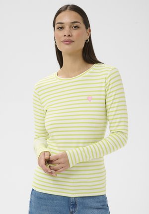 Ženska z dolgimi temnimi lasmi, ki nosi uhane v obliki obročev in belo majico z dolgimi rokavi z svetlo zelenimi črtami ter majhnim roza srčnim simbolom.