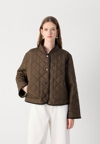 Veste matelassée marron avec un col haut, des finitions noires contrastantes, des boutons sur le devant et des poches latérales. Matériau léger avec une texture douce.