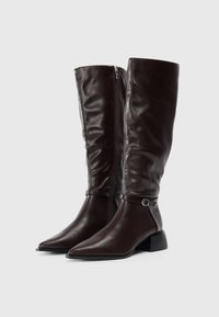 Bottes en cuir marron foncé, hautes, avec fermeture éclair sur le côté, bouts pointus, petits talons carrés, et une fine sangle avec une petite boucle au-dessus de la cheville.