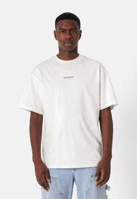 Camiseta de algodón blanca con un corte relajado, mangas cortas y un pequeño logo dorado "SIXTHJUNE* PARIS" en el pecho.