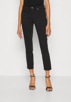 Jeans negros recortados de corte ajustado, con cierre de botón, bolsillos frontales y textura suave. Con tacones negros de tiras.