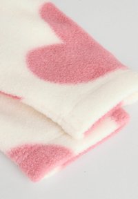 Couverture en polaire douce de couleur blanche avec de grands motifs de cœurs roses. Les bords sont soigneusement finis, mettant en valeur une texture moelleuse et des couleurs vives.