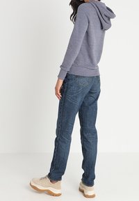 Szara bluza z kapturem z prążkowanymi mankietami, zestawiona z ciemnoniebieskimi jeansami i beżowymi trampkami z teksturowanym wzorem i masywną podeszwą.