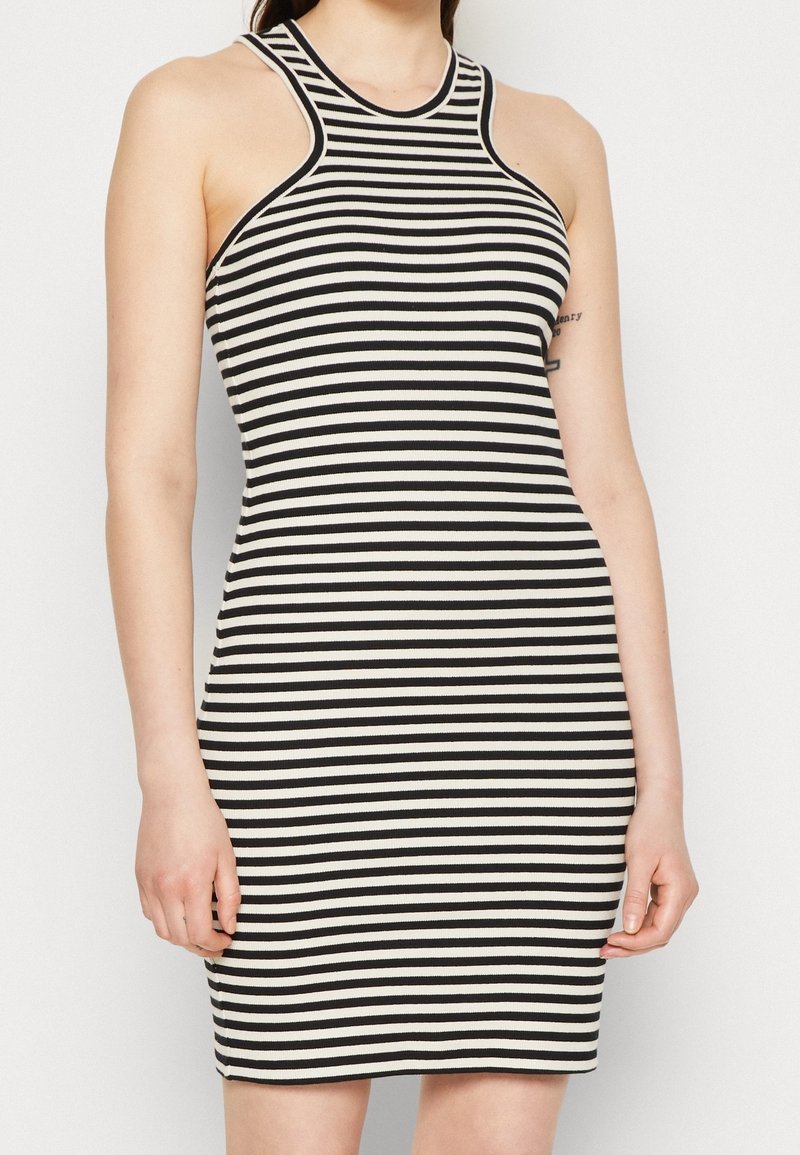 Černobílé pruhované šaty s vysokým výstřihem, bez rukávů a s přiléhavým střihem. Žebrovaná textura zvyšuje vizuální zajímavost.