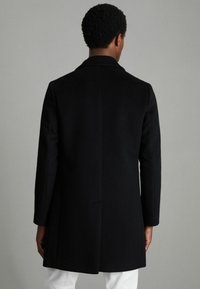 Cappotto in misto lana nera con una texture liscia, design a un bottone, colletto a scollo a V e taglio medio, con una cucitura centrale sul retro.