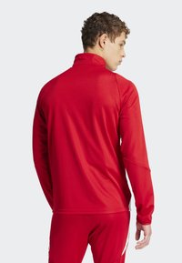 Red athletic jacket with a high collar, smooth texture, long sleeves, and stitching details. The fit is close to the body.
