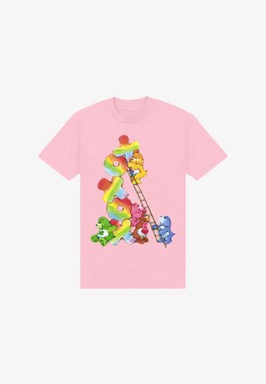 Roze t-shirt met kleurrijke Care Bears die een ladder beklimmen, leunend tegen gestapelde regenboog-puzzelstukken die het woord "toy" vormen.