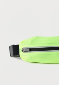 Λουμινέζον πράσινο τσαντάκι μέσης από μαλακό ύφασμα, με μαύρη τσέπη με φερμουάρ και ρυθμιζόμενο μαύρο λουρί για ασφαλή στερέωση.