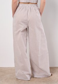 Pantalons à larges rayures en tissu beige clair et blanc cassé, dotés d'une taille élastique et de poches latérales, avec une finition lisse et texturée.