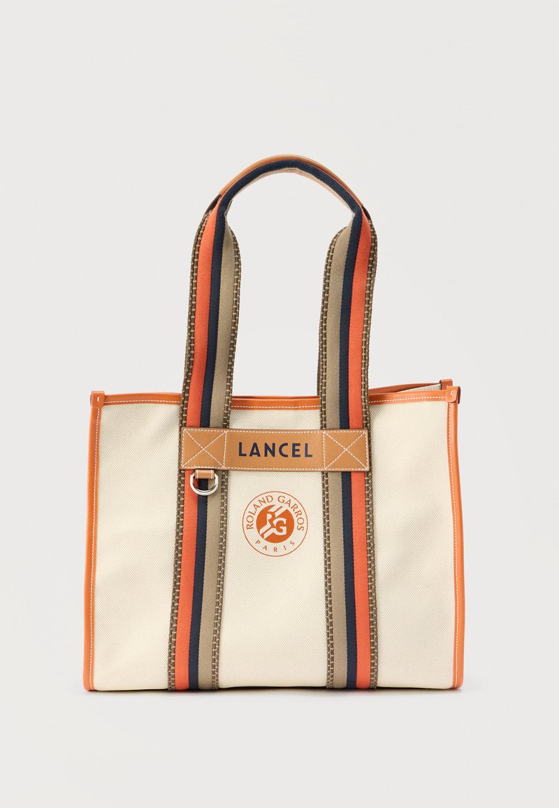 Καμβά τσάντα ώμου σε μπεζ χρώμα με πορτοκαλί και ναυτικό ρίγες στα χερούλια, διακοσμημένη με καφέ δερμάτινη ετικέτα που φέρει την επιγραφή "LANCEL" και στρογγυλό λογότυπο με το κείμενο "ROLAND GARROS".