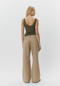 Khaki színű, laza szárú nadrág és olíva zöld ujjatlan felső. A felső hátul kerek kivágású; a nadrág hátsó zsebekkel rendelkezik és kényelmes fazonú. Simább textúra.