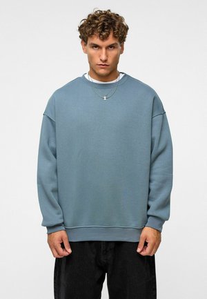 Lichtblauwe sweatshirt van zachte stof, met een ontspannen pasvorm, ronde halslijn en ribgebreide manchetten, gecombineerd met donkere jeans.