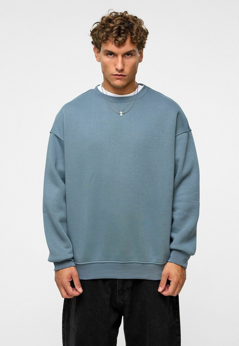 Lichtblauwe sweatshirt van zachte stof, met een ontspannen pasvorm, ronde halslijn en ribgebreide manchetten, gecombineerd met donkere jeans.