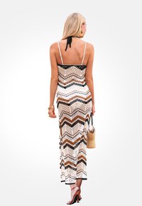 Robe maxi en tricot avec un motif en zigzag dans des tons de brun, noir et blanc. Présente des fines bretelles et des fentes sur les côtés. Accessoirisée avec un petit sac tissé.