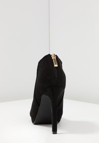 Černé semišové lodičky s špičatou špičkou, vybavené zadním zipem a štíhlým stiletto podpatkem. Hladká textura a minimalistický design.