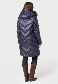 Gevoerde jas in donker marineblauw met een chevrondesign, voorzien van een grote capuchon, lange mouwen en een knie-lange snit, gedragen met bruine cowboylaarzen.