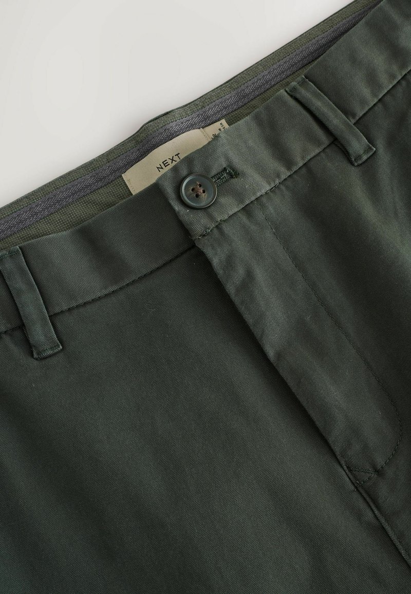 Dark green chinos with a flat front, button closure, and belt loops. Smooth fabric with a slight sheen; tag displays "NEXT."
