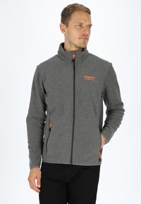 Gray fleece jacket with high collar, orange zipper accents, zippered side pockets, and a logo on the chest. Smooth texture.