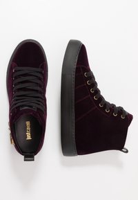 Para ciemnofioletowych, welurowych sneakersów typu high-top z czarną platformą i czarnymi sznurówkami, z logo Just Cavalli wewnątrz.