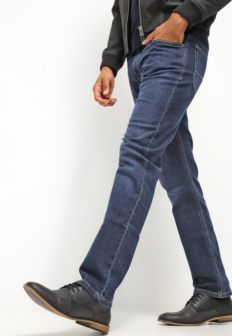 Dunkelblaue Denim-Jeans mit geradem Schnitt, die ein dezentes strukturiertes Muster und kontrastierende Nähte aufweisen, getragen mit schwarzen Lederschuhen.