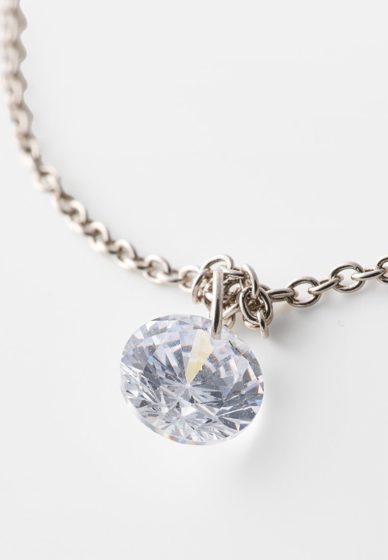 Collar de cadena de plata con un colgante ovalado de cristal transparente, que presenta facetas que reflejan la luz, mostrando un acabado limpio y pulido.