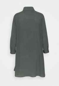 Camicia verde scuro con pois bianchi, maniche lunghe e colletto, caratterizzata da una vestibilità ampia e un tessuto leggero.