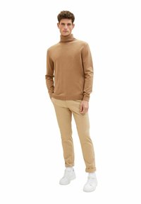 Ljusbrun polokrage-tröja, mjuk textur, smal passform. Kombinerad med beige chinos och vita sneakers. Enkel design, inga mönster eller detaljer.
