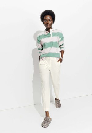 Polo à manches longues rayé vert et rose, pantalon crème et chaussures à enfiler imprimé léopard. Tissu lisse et coupe décontractée.