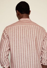 Camisa de botones a rayas en tejido suave; presenta una base rosa claro con rayas verticales blancas y mangas enrolladas.