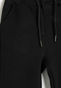 Svarta vävda joggers med elastisk midja, snöre, framfickor och en strukturerad yta.