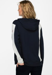 Marineblå hættetrøje med hvide sidepaneler, der har en kangaroo-lomme og justerbar snor. Blødt stof med en glat tekstur.