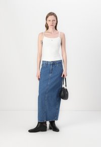 White sleeveless top, blue denim maxi skirt, black ankle boots, and a small black handbag with a chain detail.