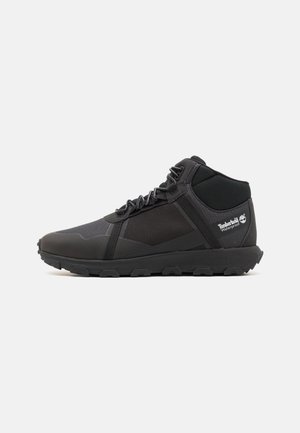 Zapatillas negras de altura media con una mezcla de texturas suaves y de malla. Cuentan con suela de goma, talón reforzado y el logo de Timberland en el lateral.