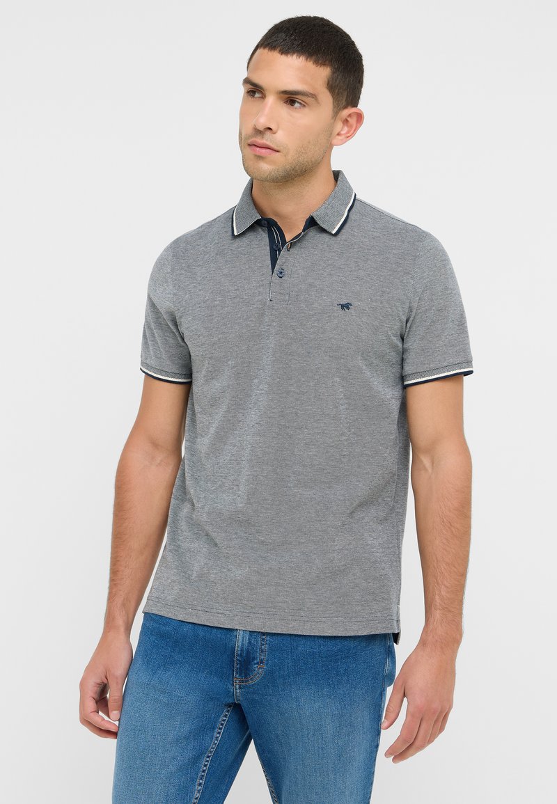 Szary podkoszulek z granatowym kołnierzykiem i paskowanymi akcentami, z krótkimi rękawami i małym logo na piersi. Noszony z niebieskimi dżinsami.