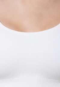 Witte, gladde mouwloze top met een ronde halslijn. De stof lijkt rekbaar met subtiele patronen. Geen zichtbare hardware of accenten.