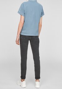 Vaaleansininen lyhythihainen polo-paita yhdistettynä tummanharmaisiin kerrospolkimiin ja valkoisiin lenkkikengiin. Yksinkertainen muotoilu, ei näkyviä kuvioita.