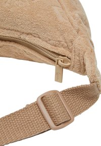 Teksturert beige veske med glidelåsslukking, som har et stoffbånd og en metallkrok. Designet er enkelt og kompakt.