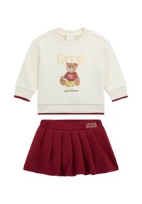 Maglione crema con accenti bordeaux, caratterizzato da una grafica di un orso e il testo "GUESS", abbinato a una gonna plissettata bordeaux con logo ricamato.