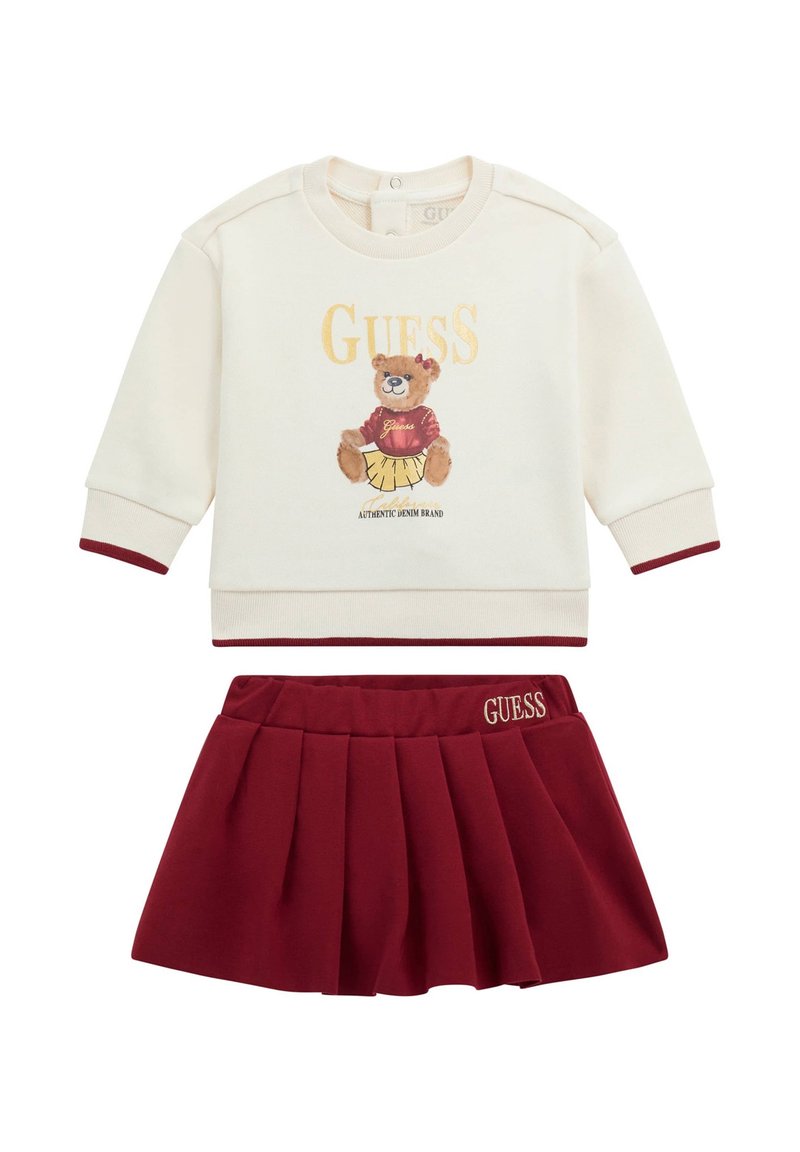 Maglione crema con accenti bordeaux, caratterizzato da una grafica di un orso e il testo "GUESS", abbinato a una gonna plissettata bordeaux con logo ricamato.