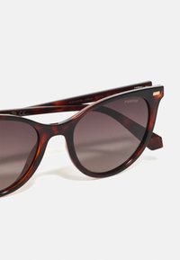Ochelari de soare tip cat-eye din tortoise shell, cu lentile în degrade întunecat și accente aurii subtile. Realizați din plastic, cu o textură netedă și rame rotunde.